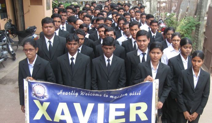 A group of students standing together on the campus of XCHM, holding a banner.